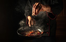 Cooking fresh vegetables. The chef adds salt to a steaming hot pan. Grande cuisine idea for a hotel with advertising space.