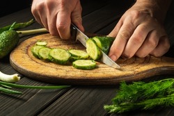 Slicing cucumbers on a cutting board. Delicious salad for dinner with fresh vegetables. Hands of a chef with a knife while cooking in a restaurant kitchen.