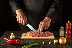 The chef cuts raw beef meat on a cutting board before baking. European cuisine. Hotel menu recipe idea.