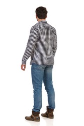 Standing young man in jeans, boots and lumberjack shirt. Rear side view. Full length studio shot isolated on white.