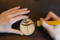 Female hands burn out a tree twig sign with soldering iron on wooden disc.