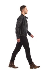 Walking man in black leather jacket and black jeans. Full length studio shot isolated on white.