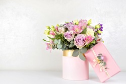 Beautiful bouquet of flowers in round box and pink gift box on a white table. Gift for holiday, birthday, Wedding, Mother's Day, Valentine's day, Women's Day. Floral arrangement in a hat box.