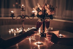 Hands man and woman holding glasses of wine having romantic candlelight dinner at table at home. Hands man and woman holding glass of wine. Concept of Valentine's day or Candlelight date at night.