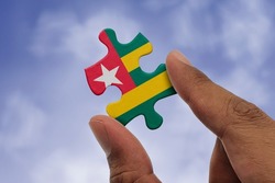 Hand holding piece of jigsaw puzzle with flag of Togo. Jigsaw puzzle of Togo flag on sky background.