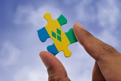 Hand holding piece of jigsaw puzzle with flag of Saint Vincent. Jigsaw puzzle of Saint Vincent flag on sky background.