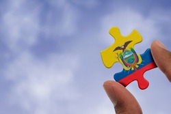 Hand holding piece of jigsaw puzzle with flag of Ecuador. Jigsaw puzzle of Ecuador flag on sky background.