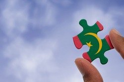 Hand holding piece of jigsaw puzzle with flag of Mauritania. Jigsaw puzzle of Mauritania flag on sky background.