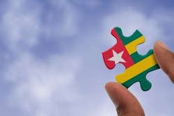 Hand holding piece of jigsaw puzzle with flag of Togo. Jigsaw puzzle of Togo flag on sky background.