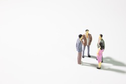 A small group of miniature businessman 
stand meeting on white background.