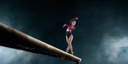 Female gymnast doing a complicated trick on gymnastics balance beam.