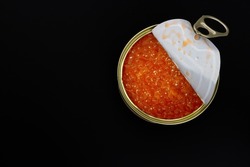 An open metal can with red salmon caviar isolated on a black background. View from above