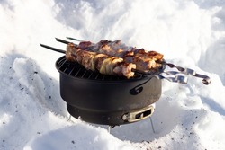 Pork on skewers on grill in winter. Winter outdoors picnic. BBQ shashlik on portable barbecue grill in the deep snow