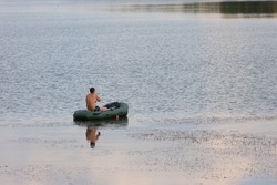 A man on a rubber boat is fishing with rods in the middle of the river in summer day