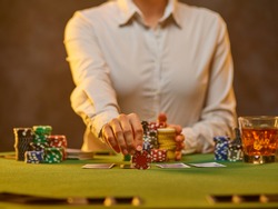 A croupier in a white uniform shirt lays out gambling chips on the table. The cards are on the table. Gambling business, pastime, leisure. Close-up. Brownish green tones.