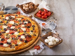Big mouth-watering pizza with ingredients in wooden bowls around it. Bright colors, light background. Restaurant dish, home cooking dish, fast food, many ingredients.
