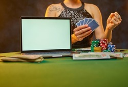On the green poker table are poker cards, chips, a laptop. Young woman holds cards in her hands. Gambling, poker. Night club, casino, gambling addiction, strategy games.