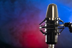 Modern professional microphone on an interesting colored background, smoke. Recording studio, vocals, television, radio broadcasting, concert, nightclub Careful viewing.
