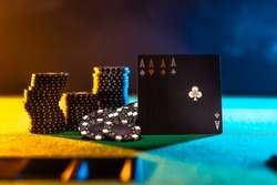 Casino, online casino. Black poker cards and stacks of black chips on a green gambling table. Multicolored background. There are no people in the photo. Night club, casino, gambling business.
