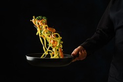 Italian pasta with greens and shrimps in a pan in a frozen flight on a black background. Sea food. Restaurant, hotel, banquet, home cooking. Healthy vegetarian food, healthy lifestyle.