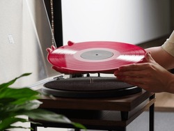 Red vinyl record in female hands. The player is on the table. Room interior. Close-up. Music equipment, music, songs, sound recording.