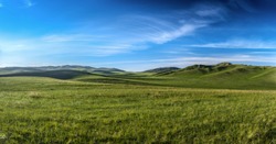 Distant hills. Hilly steppe. Curvy hills. Blue sky and grass. Beautiful plain. Sunny day and hills. Lowland. Hilly horizon.