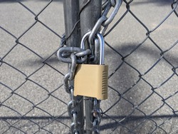 Close up of a yellow padlock and chain keeping a chainlink fence sealed