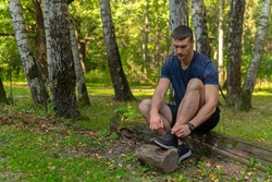 Man tying his shoelaces in the park outdoors, around the forest, oak trees green grass young enduring athletic athlete. healthy runner forest, lifestyle jogger young motion, jogging wellbeing. Autumn