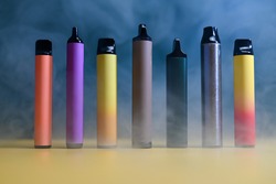 multicolored vape electronic cigarettes on dark green background in smoke. High quality photo