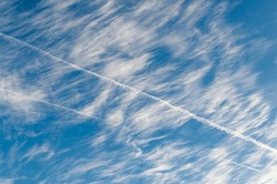 Cirrus clouds ruffled by storm against blue sky with contrail