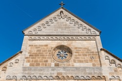 West facade of St. John's Church in Swabian Gmüne with round Romanesque stained glass window, round arch friezes and pilaster strip in sunshine and blue sky