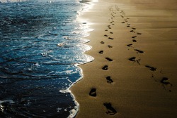 Two pairs of footprints in the sand on the beach and incoming waves