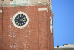 side wide of a gold round classic time clock with a brick wall building church and a blue even sky on the background 