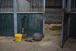 Empty horse stable stall. To be prepared for horses with straw to put as bedding. Fork, brush, shovel, feed bowl and water bucket at the stable entrance. 