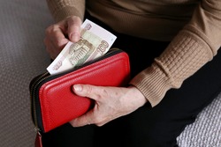 Elderly woman takes out russian rubles from her wallet, wrinkled female hands closeup. Concept of poverty in Russia, pension payments, pensioner