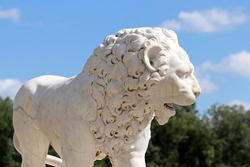 Stone lion decorating summer park. Marble sculpture on blue sky and green trees background