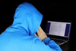 Cybercrime, hacking and internet. Man in blue hoodie sitting with laptop on black background, concept of torrent piracy and web surfing