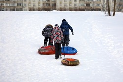 Children having fun on snow tubes, tubing in winter city. Kids climb the slide to roll down it
