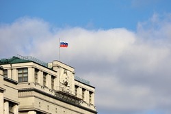 Russian flag on the parliament building in Moscow on background of blue sky and white clouds. Facade of State Duma of Russia with soviet coat of arms, russian authority