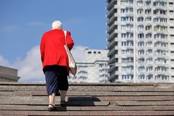 Elderly woman in summer clothes up the steps from the underpass on city buildings background, old age concept
