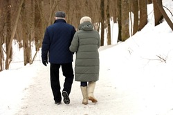Elderly woman and man walking in winter park, rear view. Old couple in warm clothes during snow weather, concept of old age