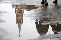 Moscow Red square during rainy weather. Reflection of Kremlin tower and walking people in a puddle of water, melting snow