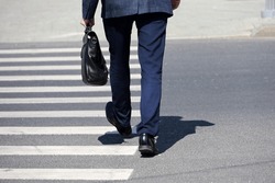 Man with briefcase wearing business suit crossing the street at a crosswalk. Male legs on the pedestrian crossing