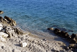 Coast with white pebbles and white rocks next to the blue wavy sea in untouched nature