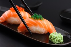 Salmon sushi nigiri in chopsticks over black background