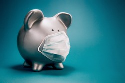 Close up of piggy bank, wearing protective face mask, isolated on blue background. Money saving concept in time of coronavirus pandemic.