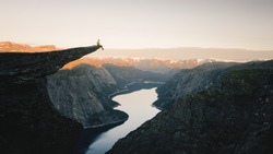 Man traveler on Trolltunga rocky cliff edge in Norway mountains Travel Lifestyle adventure emotional concept extreme vacations outdoor sunrise, tourist sitting alone
