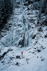 Hiker with red jacket watching winter Stuibenfall waterfall in Otztal, Austria is the longest waterfall (159 m) in Tirol. Man hike.