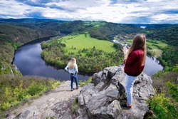 Young woman with camera take photo girl. Blogger photoshoot concept. Tourist travels. Beautiful outlook on the Vltava river, mountains and hills during sunset from the the viewpoint Altan.