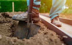 Male foot wearing a rubber boot digging an earth in the garden with an old spade close up. Soil preparing for planting in spring. Agriculture and people concept 